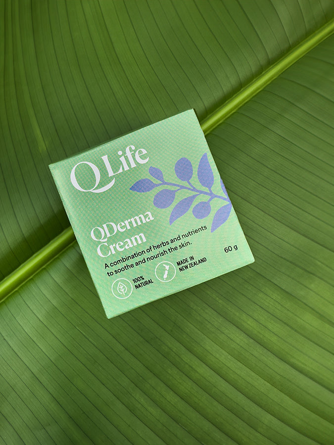 Q Life QDerma Cream box on a green leaf, highlighting the product's natural ingredients.
