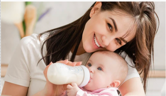 A smiling mother holding and feeding a baby with a bottle.